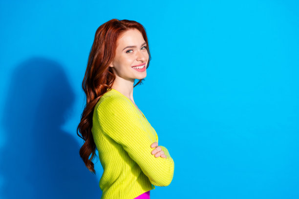 侧面照片，漂亮的女孩，姜黄色发型，穿着黄色开衫，双臂交叉，背景为蓝色。图片下载