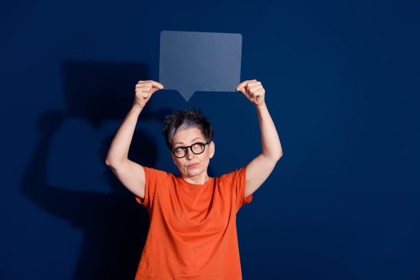 吸引人的老年女士的照片肖像，表情怀疑，穿着时尚的橙色衣服，背景为深蓝色。图片下载