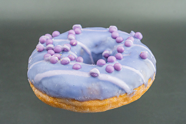 一款带有紫色糖屑的釉面甜甜圈在浅色背景下显得格外突出，这是一张简单明了的照片。图片下载