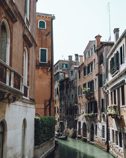 迷人的照片展示了意大利威尼斯狭窄的街道，标志性的巷子两旁是古老的建筑、色彩斑斓的外立面和生机勃勃的花朵。图片下载