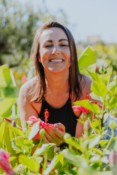 一位女性在花园里微笑着，手中拿着一朵粉色的花，竖版照片。图片下载
