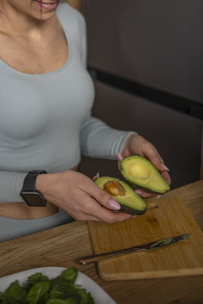 可爱的女人在厨房台面上切牛油果，准备健康的绿色排毒饮料，特写照片。图片下载
