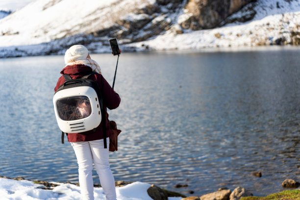背包里装着猫的女性在拍摄山湖的照片图片下载