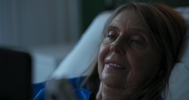 照片捕捉到一位住院的老年女士，专注于在平板电脑上阅读新闻文章，保持信息灵通。图片下载