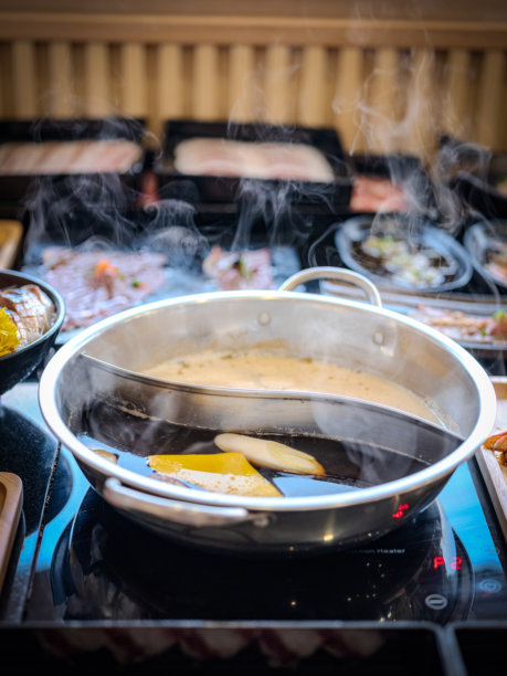 特写照片展示一个不锈钢火锅，分为两部分，一侧是浓郁的深色汤，另一侧是清淡的清汤。图片下载