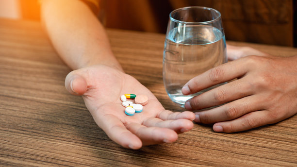 男性手握着膳食补充剂，维生素C、B、鱼油，并握着一杯水，手掌上的膳食补充剂或药丸特写照片图片下载