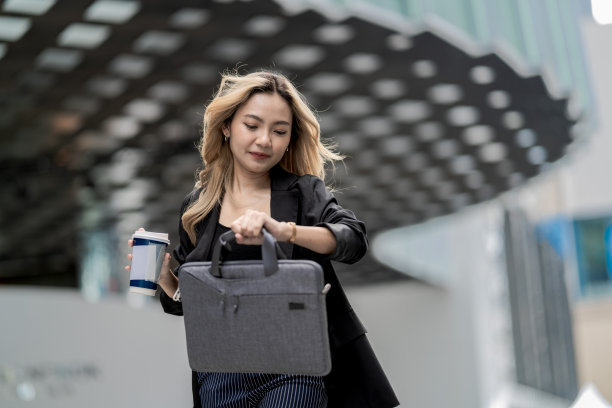 一位穿着商务服装的女性正在看手表，手中拿着咖啡杯，象征着高效和时间管理。这张图片代表了繁华城市中充满活力的工作与生活平衡。图片下载