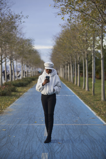 一组黑女性穿着白色时尚外套和帽子在公园里使用手机的照片系列图片下载