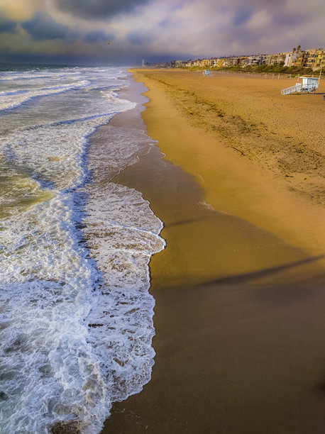 曼哈顿海滩海岸的肖像风格照片，背景是戏剧性的天空和海滩房屋，海浪拍打着岸边。图片下载