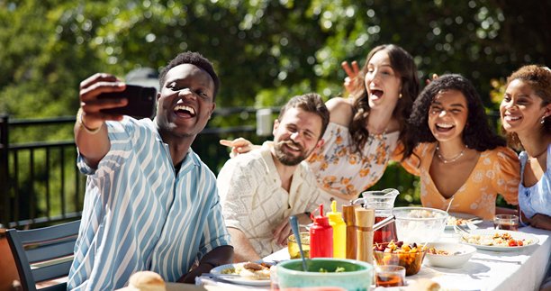 朋友们在户外庆祝新年，享用午餐并微笑自拍，社交聚会或更新个人资料照片。快乐的回忆，多元化的人群，或在露台上与食物一起拍摄的节日派对照片。图片下载