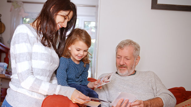 多代家庭坐在家里的沙发上查看照片图片下载