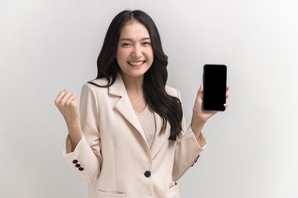 年轻美丽的亚洲女性的肖像照片，感到快乐或惊讶，手中拿着黑色空白屏幕的智能手机，背景为白色，可用于广告或产品展示概念。图片下载