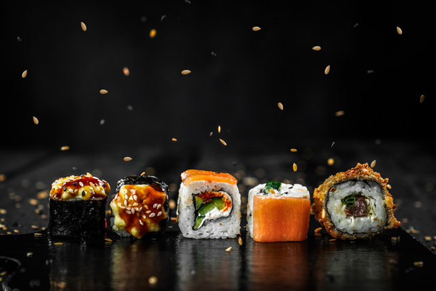 创意照片：寿司卷漂浮，海苔棒和芝麻在黑色背景上，餐厅菜单。图片下载