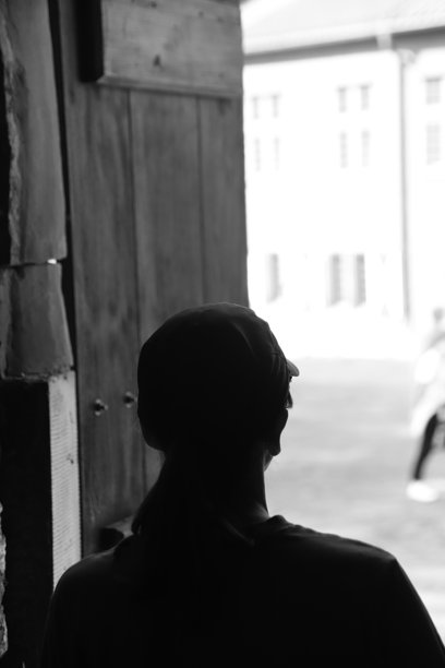 波兰格但斯克的维斯鲁维斯特堡：一位戴着棒球帽的女性在木百叶窗的窗户旁凝视，黑白照片图片下载
