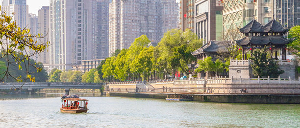 美丽的全景照片，展示了一只小木船在成都的锦江河上经过鹤江亭，成都是一座以悠闲生活方式而闻名的四川和中国的超级公园城市。图片下载