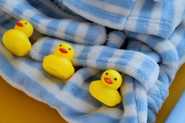 黄色和白色背景上的护肤产品照片。旁边有一只明亮的橡皮鸭。婴儿的蓝白色浴袍。图片下载