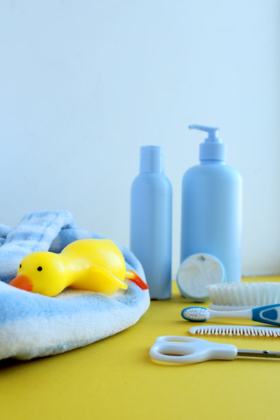 黄色和白色背景上的护肤产品照片。旁边有一只明亮的橡皮鸭。婴儿的蓝白色浴袍。图片下载
