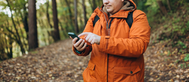 年轻的白人30多岁男子背包客在森林中用智能手机寻找信号。公路旅行、交通、旅游、科技和人们的概念。高质量照片图片下载