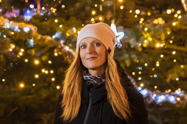 戴着帽子和夹克的美丽微笑女性肖像，背景模糊的灯光。圣诞节，城市夜生活照片。图片下载