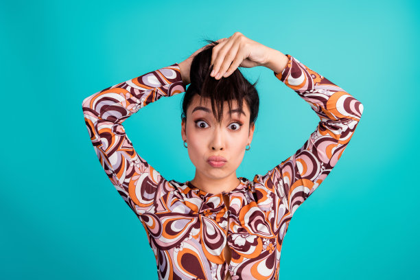 可爱的年轻女士在青色背景下困惑地拉扯头发，穿着时尚的彩色衣服的照片肖像图片下载