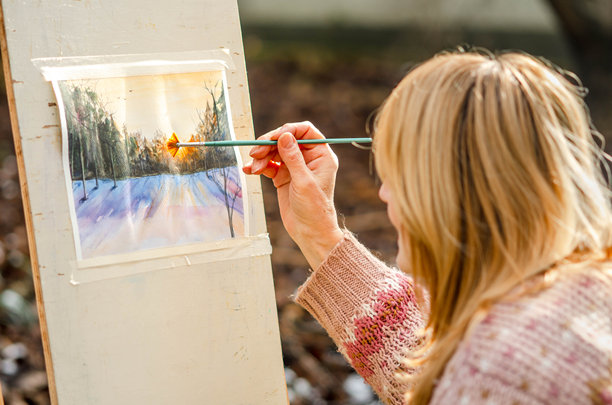 冬季户外，一位年长女性正在绘制水彩画，捕捉着雪地上宁静美丽的风景。图片下载
