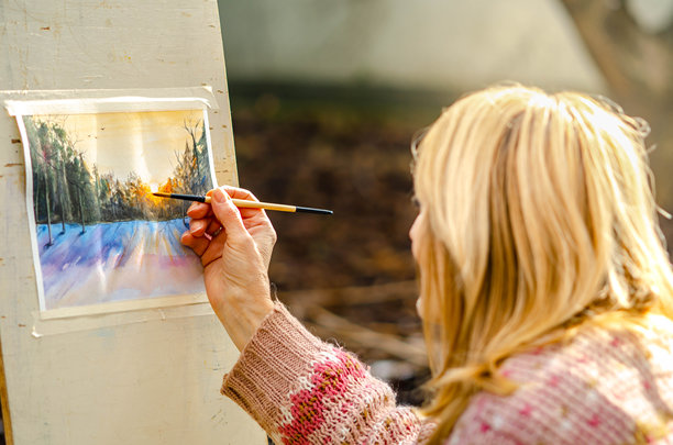 冬季户外，一位年长女性正在绘制水彩画，捕捉着雪地上宁静美丽的风景。图片下载