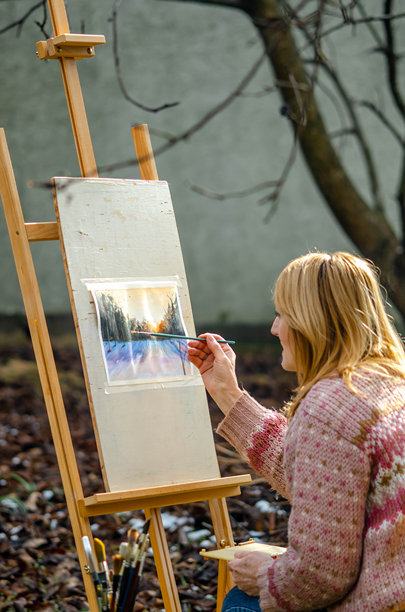 冬季户外，一位年长女性正在绘制水彩画，捕捉着雪地上宁静美丽的风景。图片下载