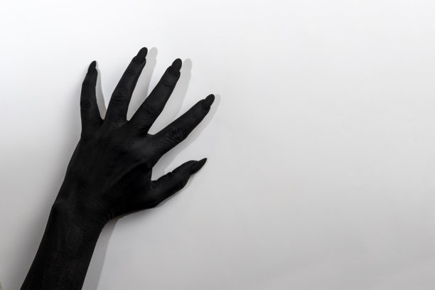 黑色长指甲的手。概念照片，女人的手涂成黑色，正在墙上移动。图片下载