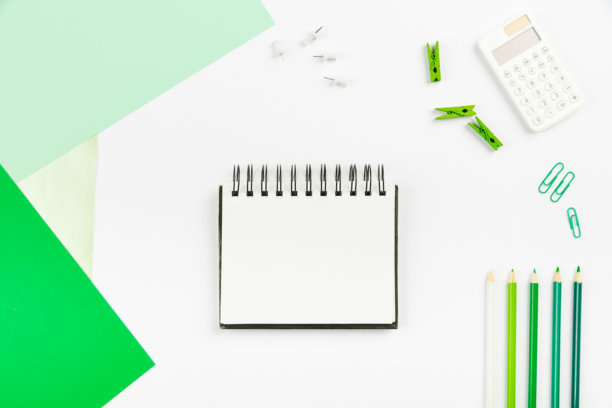 多种办公文具的集合照片，包括钢笔、铅笔、记事本、笔记本、尺子、订书机、剪刀、夹子、回形针、文件夹和剪贴板，摆放在桌子上。图片下载