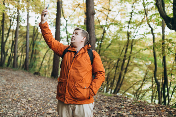 失落而愤怒的金发男子在森林中独自徒步旅行时迷路，无法在手机上找到网络连接。公路旅行、交通、旅行、科技和人类概念。高质量照片图片下载