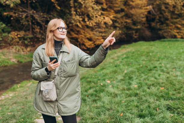 金发女徒步旅行者手持智能手机，指向河边的某个地方。旅行、科技与放松的概念。高质量照片。图片下载