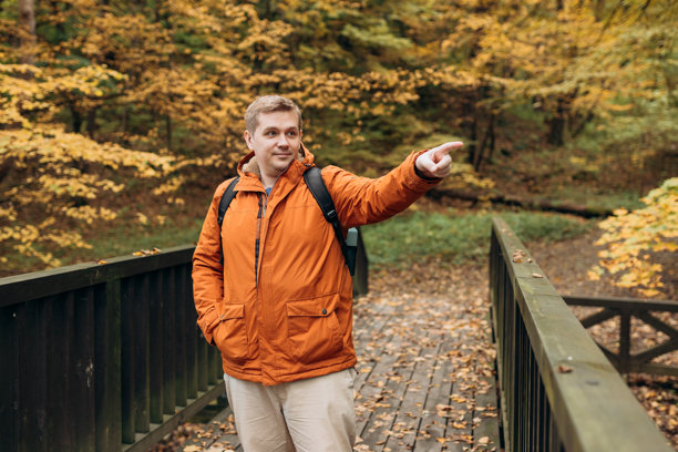 户外背着背包的金发男性指着前方，他正在林地中徒步旅行。积极的生活方式概念。旅行、旅游和人群横幅。高质量照片图片下载