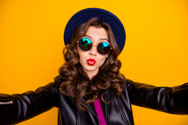 特写照片，浪漫的女孩自拍，向她的男朋友和粉丝送吻，穿着黑色皮革服装，背景为黄色。图片下载