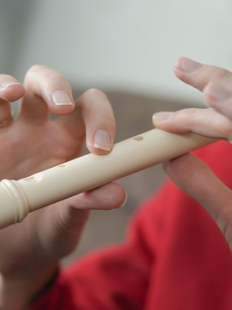 特写镜头展示音乐家手中演奏白色直笛的细节，背景为鲜艳的红色，突显出音乐表达所需的精细指法。竖版照片图片下载