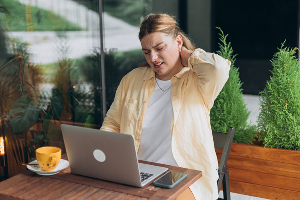 在户外坐在桌子前的30岁女性，因过度学习和颈部疼痛而感到不适，面露压力，正对着笔记本电脑。高质量照片。图片下载