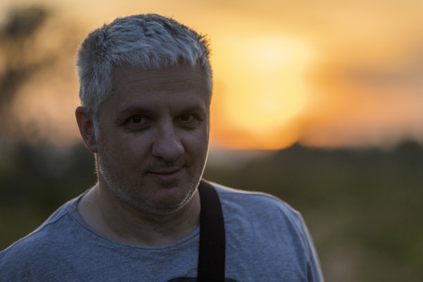 一位约50岁、头发花白的成熟男性的照片。该男子为摄影师摆姿势。照片在逆光下拍摄，背后是美丽的日落。肖像看起来有些像剪影。图片下载