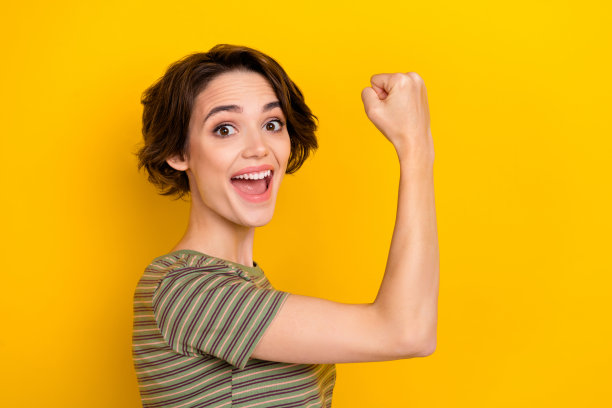 年轻漂亮女孩的特写照片，举起拳头庆祝比赛胜利，背景为黄色。图片下载