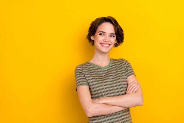 特写照片：年轻可爱微笑的小女孩双手交叉，自信地看向空旷的地方，友好地站在黄色背景前。图片下载