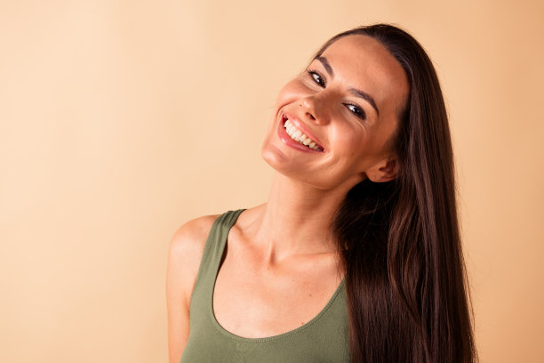 漂亮年轻女孩的照片肖像，灿烂的微笑，模特没有修饰，穿着时尚的卡其色内衣，背景为米色。图片下载