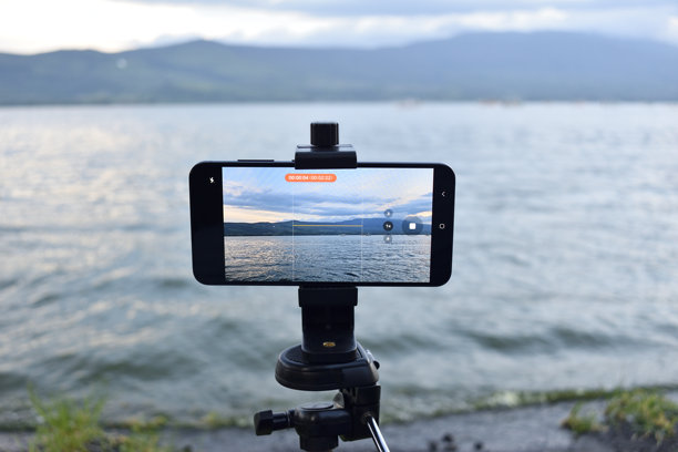一部手机安装在三脚架上，显示着卡希希特兰湖的图片。图片下载