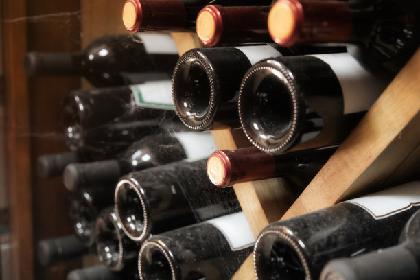 这张图片展示了一个酒架或酒窖的特写视图，几瓶酒整齐地堆放和排列。瓶子呈现出独特的深色玻璃，可能表明它们装的是红酒。瓶子上有金属瓶盖或封闭装置。图片下载