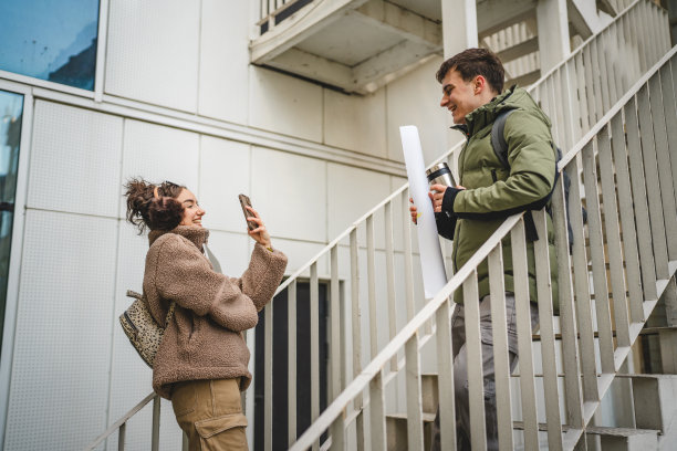 年轻女性在楼梯上用手机拍摄年轻男性的照片图片下载