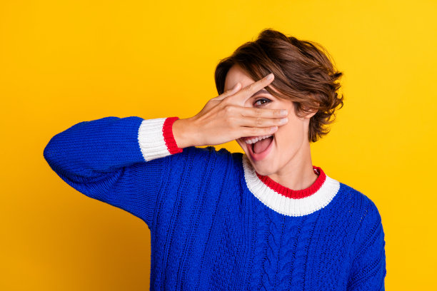 漂亮年轻女孩的照片肖像，遮住脸部，调皮地穿着时尚的蓝色针织服装，背景为黄色。图片下载