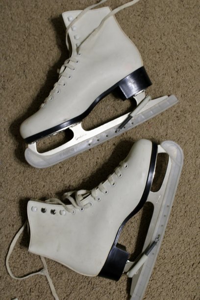 两只白色冰鞋的特写，背景为米色地板，重点展示冰鞋的金属侧面和白色皮革部分，室内，俯视角度的棕色照片。图片下载