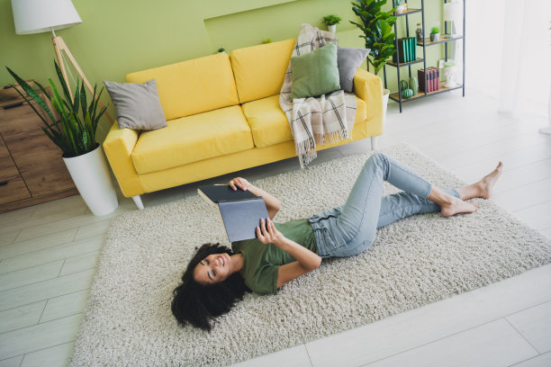 全景高角度照片，漂亮年轻女性躺在地板上阅读书籍，绿色室内公寓客厅。图片下载