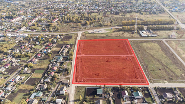 这张照片展示了一个被绿色田野和道路环绕的住宅区的俯视图。中央的红色方块在画面中格外显眼，可能是一个待开发的区域。图片下载