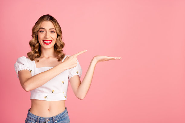 漂亮年轻女孩的照片肖像，手掌指向空白处，穿着时尚的白色服装，发型独特，背景为粉色。图片下载