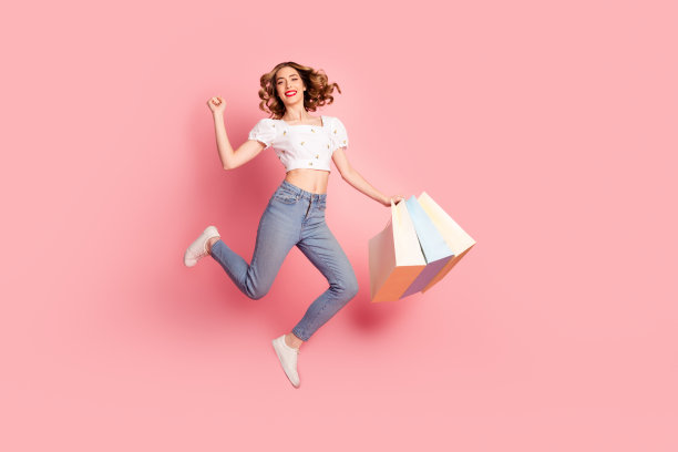 穿着白色衬衫和牛仔裤的迷人女性，手持购物袋，在黑色星期五的粉色背景上飞翔的全身照片图片下载