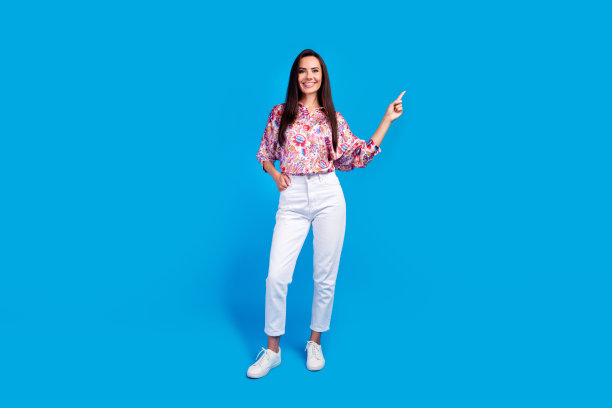 穿着印花衬衫的快乐女士在蓝色背景前指向空白区域的全身照片图片下载