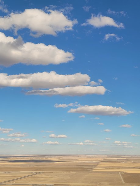 在科罗拉多州丹佛附近飞行时拍摄的抽象照片，展现了白色蓬松云朵、明亮的蓝天和赭色的风景，拍摄于二月。图片下载